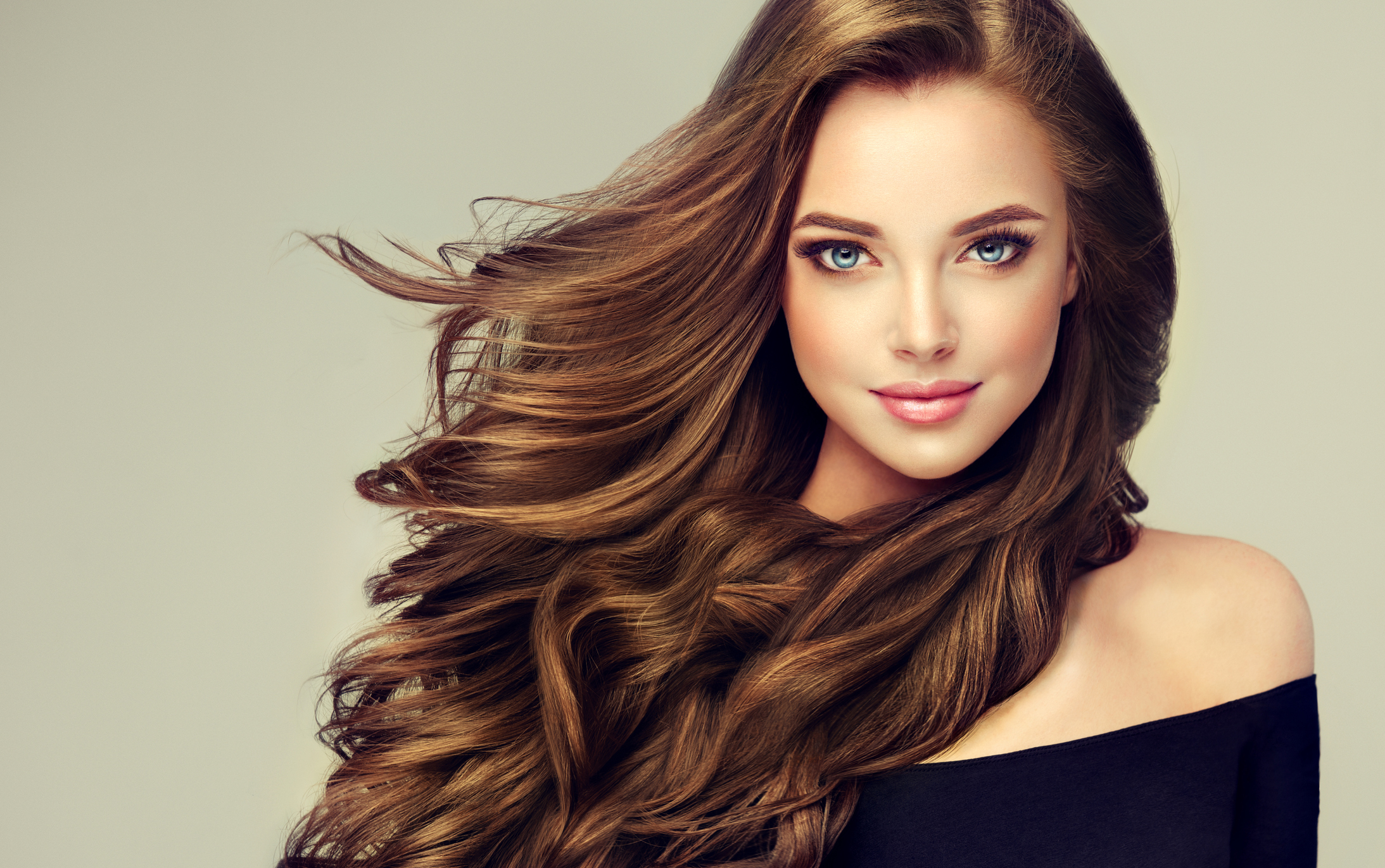 Young, brown haired woman  with voluminous hair.Beautiful model with long, dense, curly hairstyle and vivid makeup. Perfect dense, wavy,and shiny hair. Hairdressing art, hair care and beauty products.